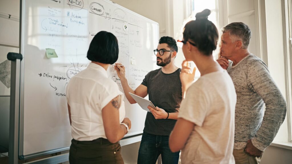 Four marketers gather around a white board and think of the best way to answer the question, "What is a marketing agency?"